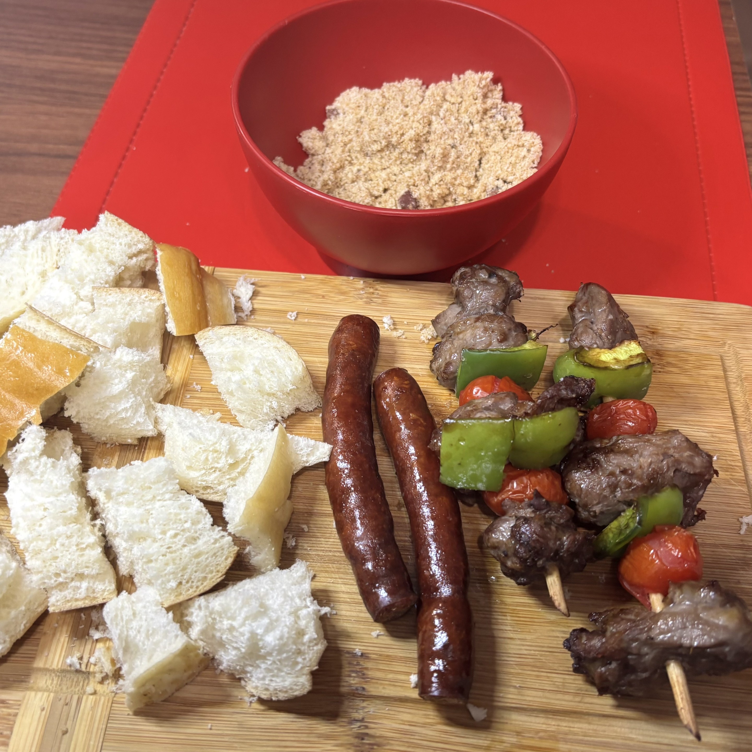 2 espetinhos de carne, pimentão e tomate, ao lado de duas linguicinhas, guarnecidos  com pão e farofa 