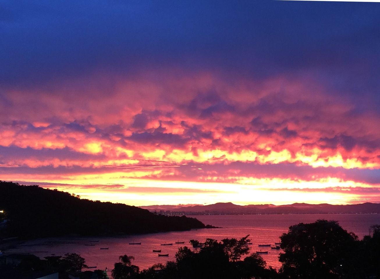 Vista de um por do sol avermelhado sobre o porto de pescadores do bairro João Paulo, em Florianópolis