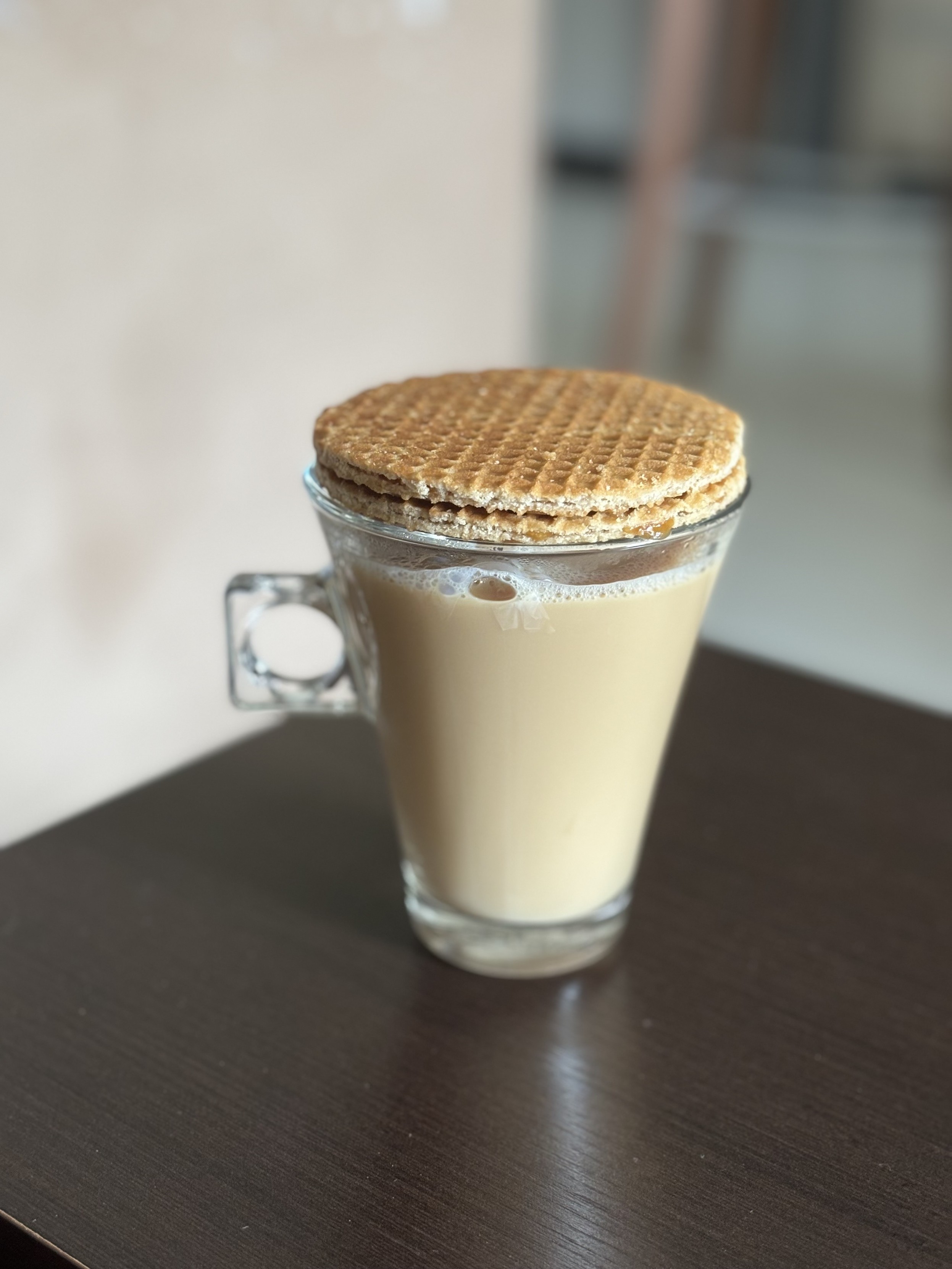Xícara transparente de café com leite, tampada por 2 biscoitos stroopwafel