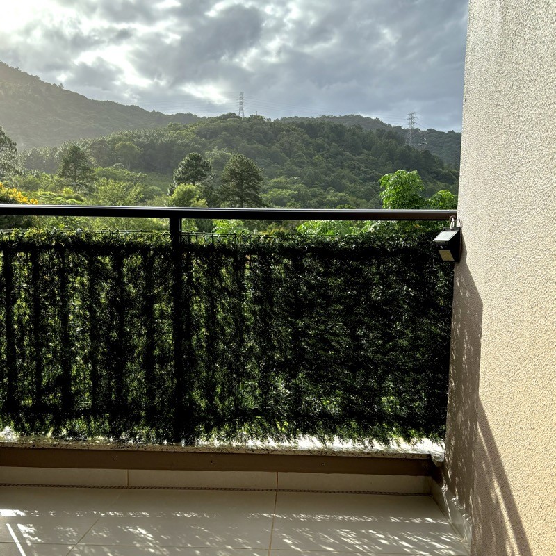 Vista da minha sacada mostrando o céu nublado sobre os morros, e o sol brilhando sobre a vegetação próxima