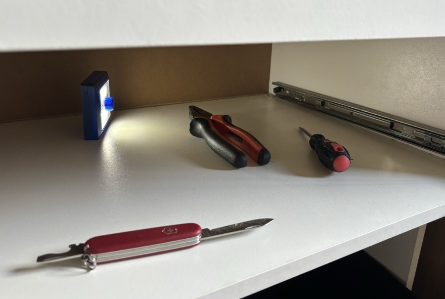 Foto do espaço normalmente ocupado pela gaveta, com uma lanterna, canivete, alicate e chave de parafusos