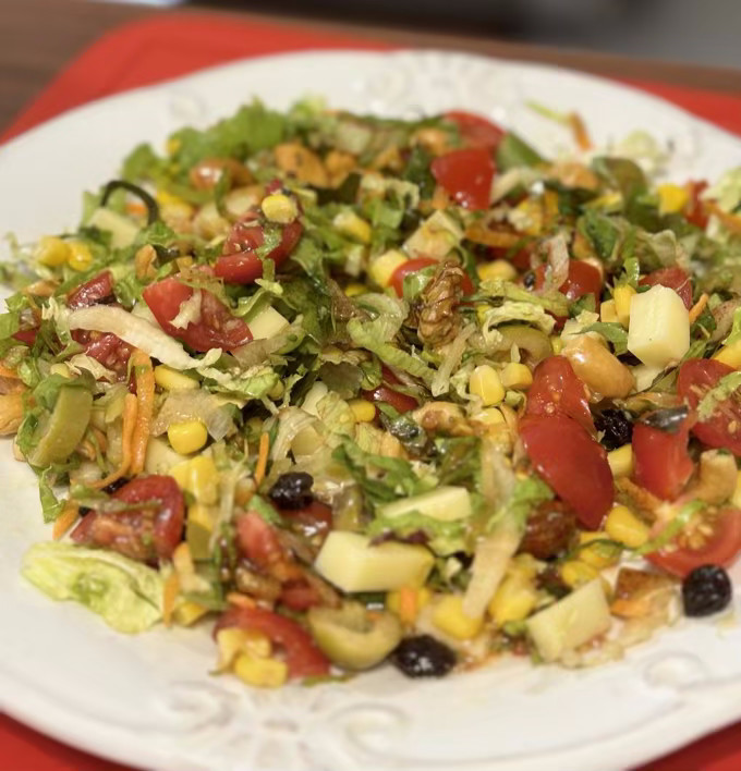 Prato de salada de folhas verdes picadas, mix de castanhas, tomate, azeitona, queijo e milho