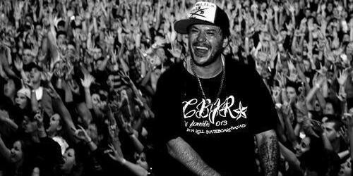 Foto em preto e branco de Chorão, sorrindo, em frente à plateia.