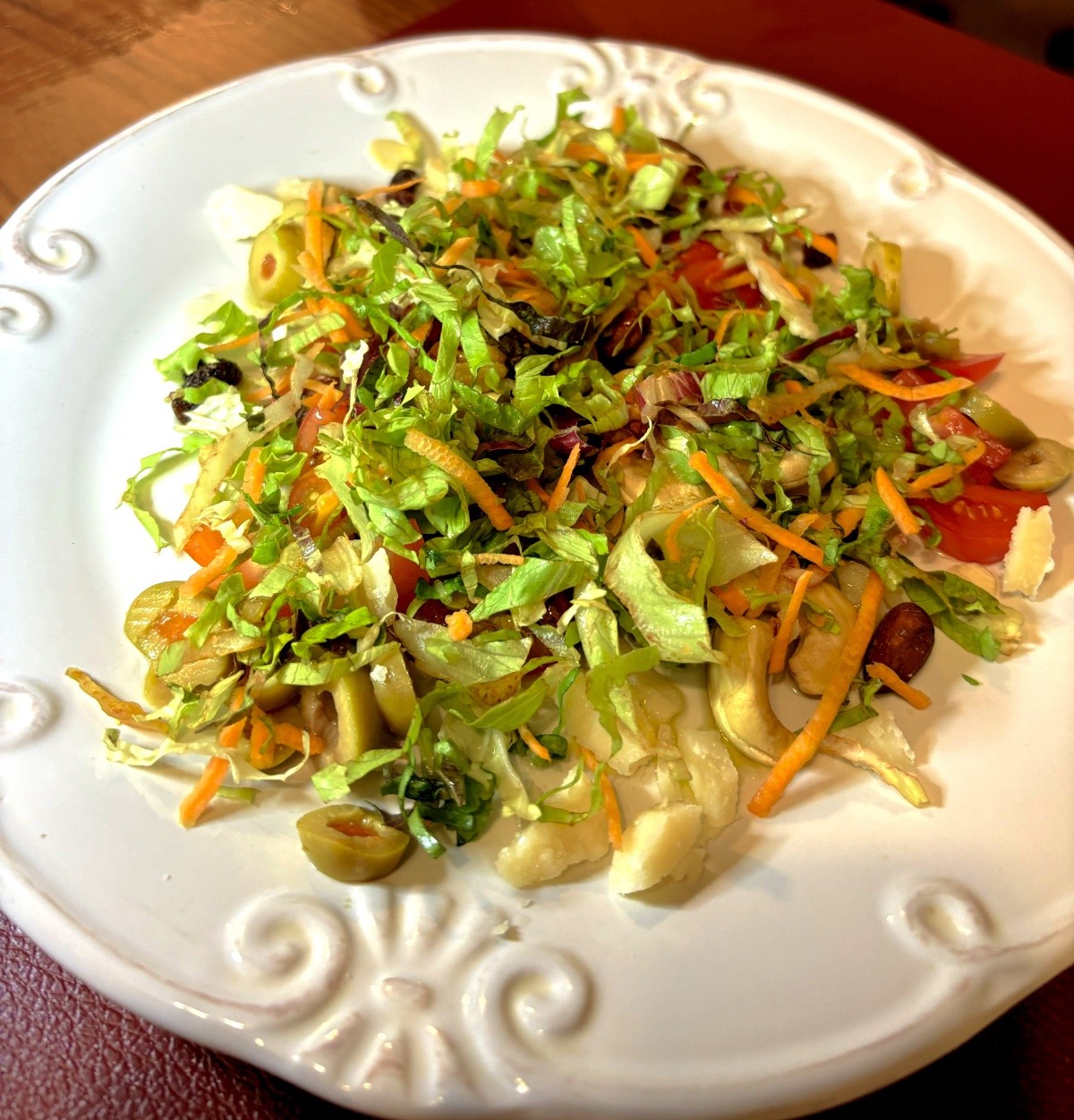 foto de um prato com salada de folhas picadas, com tomate picado, azeitonas picadas, raspas de queijo e mix de castanhas