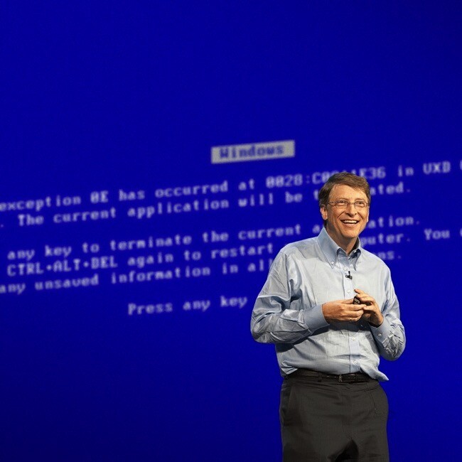 Montagem rememorando o momento, com Gates em frente a uma gigantesca tela azul do Windows