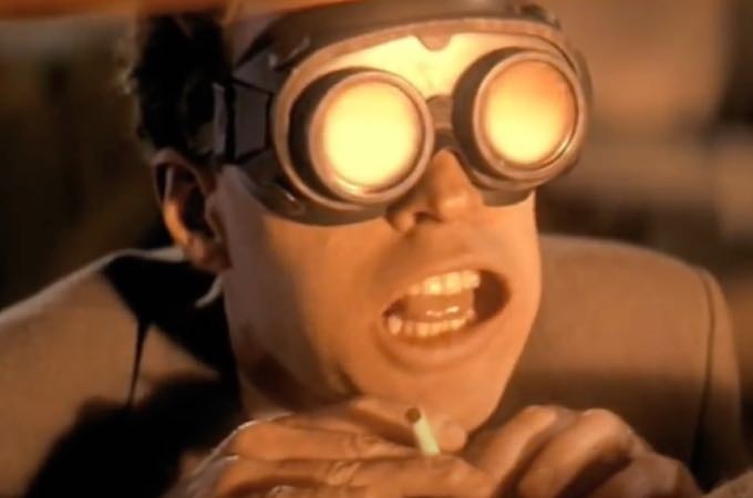 Homem usando óculos especiais, segurando um cigarro, observando uma das primeiras explosões nucleares, nos anos 1940