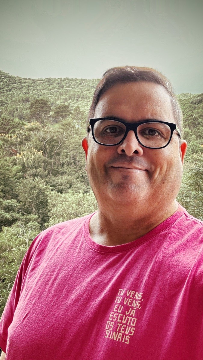 Foto minha olhando para a câmera, com a mata e o céu cinzento ao fundo, com camiseta rosa na qual se lê:<br><br>Tu vens, <br>Tu vens,<br>Eu já escuto teus sinais