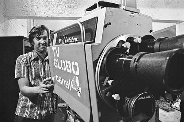 Foto em preto e branco de cameraman operando equipamento identificado como TV GLOBO CANAL 4