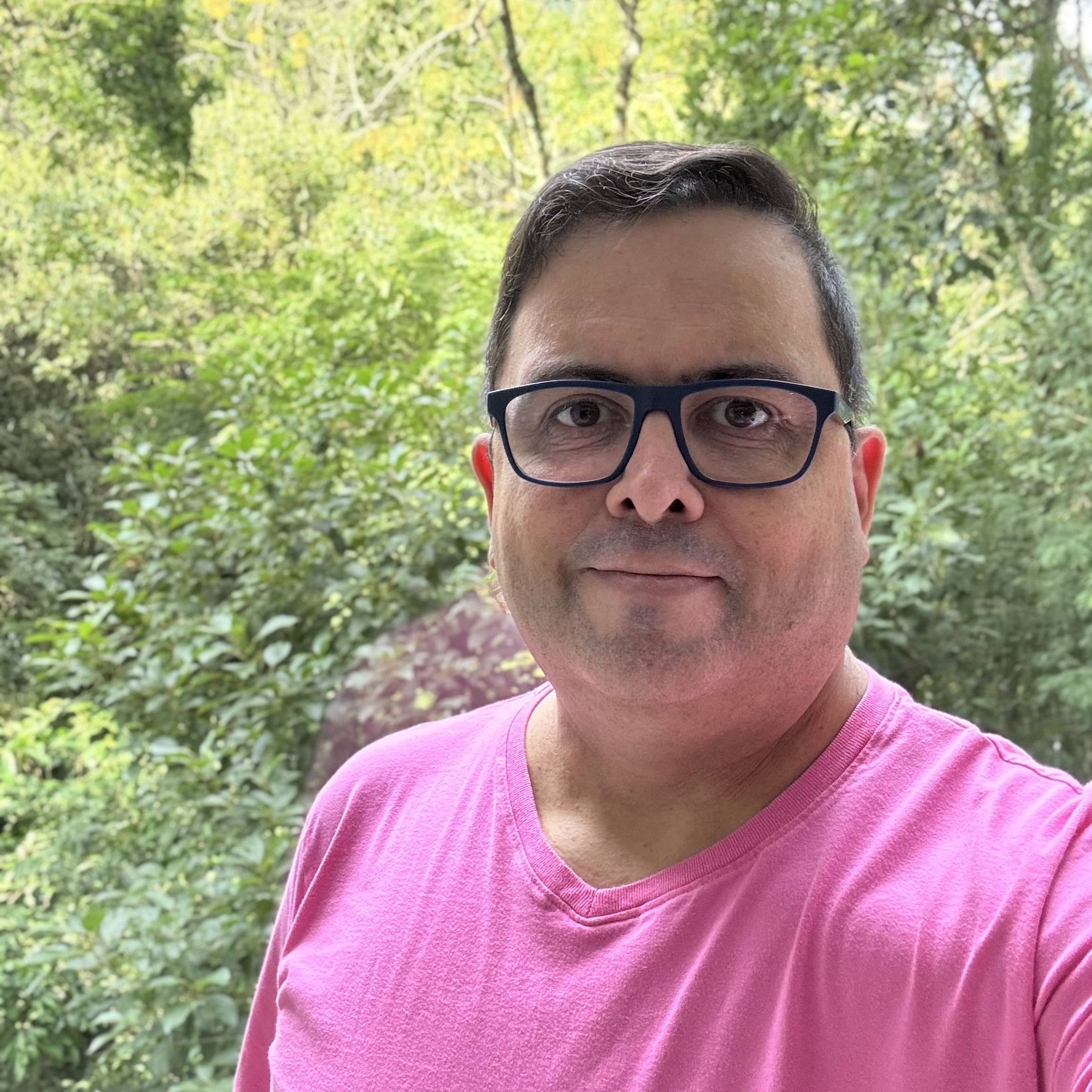 Foto minha olhando para a câmera, de camiseta rosa e com a mata ao fundo