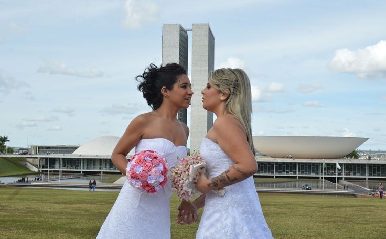 Casal celebra sua união em frente à sede do Legislativo federal, ambas de branco e com buquês