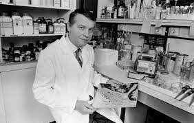 Foto em preto e branco do virologista, de jaleco, em um laboratório