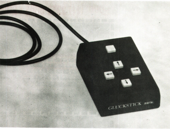 Foto em preto e branco, publicada por uma revista da época, do Gluckstick Digital, uma caixinha com 4 botões direcionais e um quinto botão, sem rótulo.