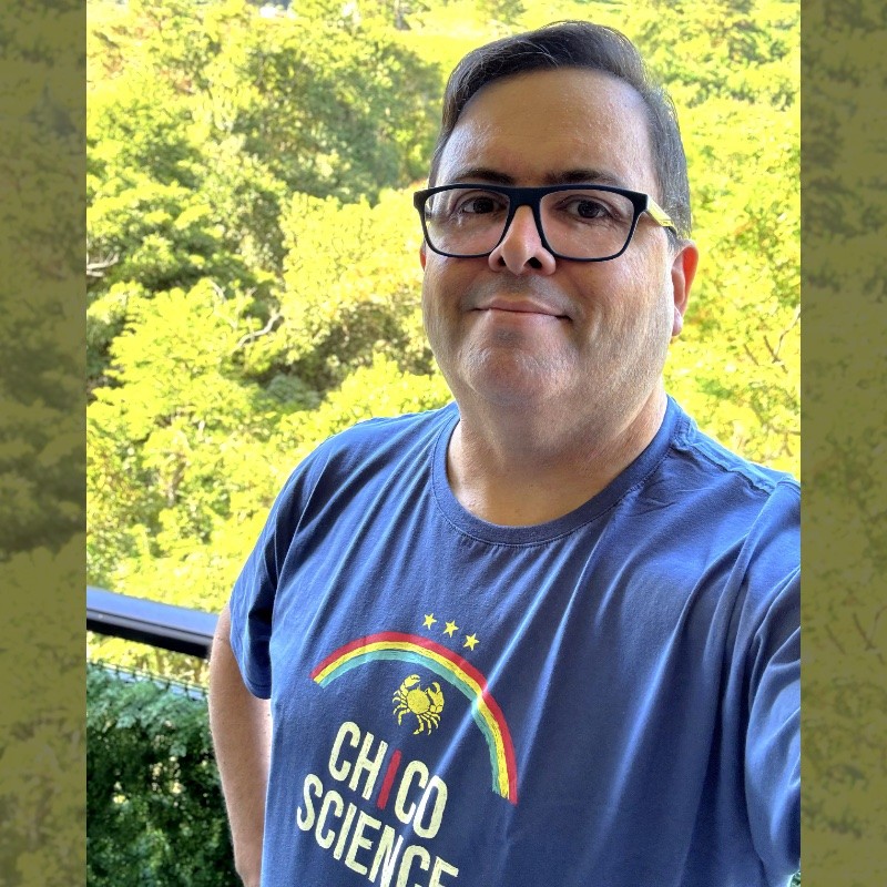 Selfie minha, com a mata desfocada ao fundo, vestindo uma camiseta com motivos da bandeira de Pernambuco e do Chico Science