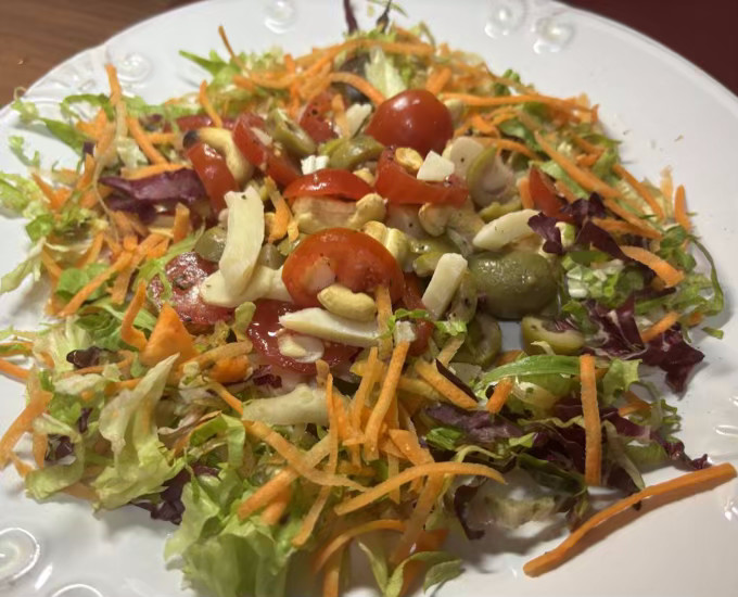 foto de um prato de salada de folhas picadas, com cenoura ralada, tomate fatiado, queijo em pedaços, azeitonas e castanhas
