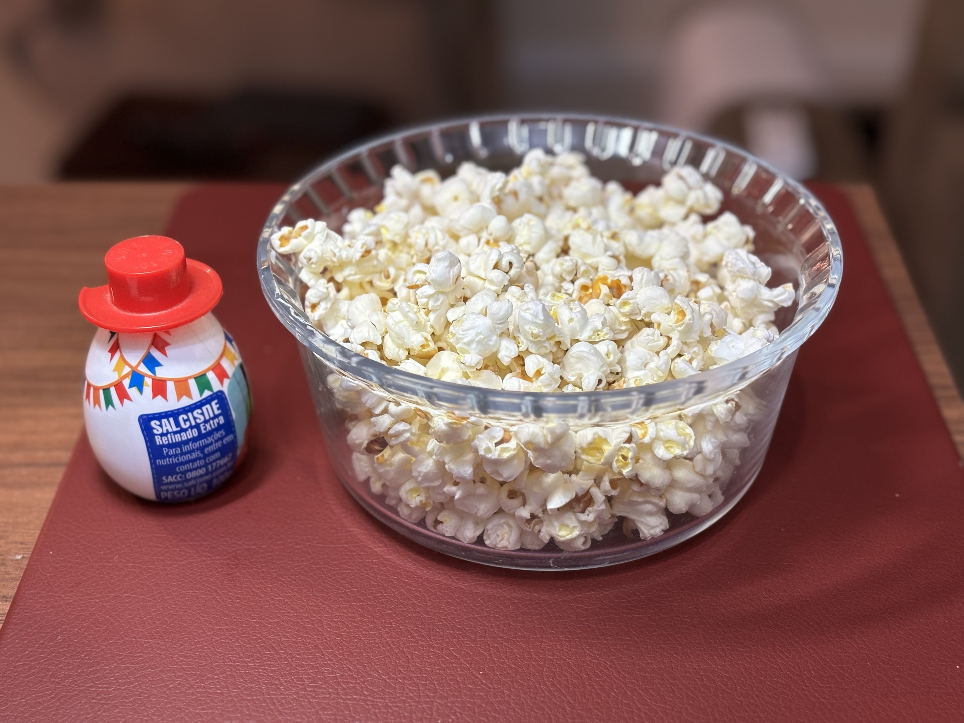 Uma travessa transparente cheia de pipoca, com um saleiro ao lado