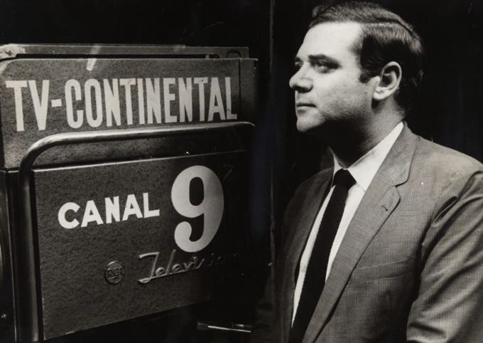 Foto em preto e branco do jornalista Heron Domingues, famoso apresentador do programa Repórter Esso, ao lado de uma câmera da TV Continental.