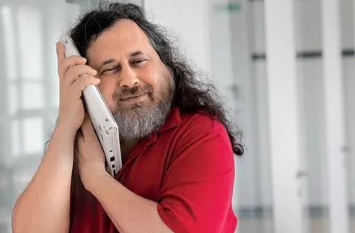 Richard Stallman com o rosto colado à parte inferior de um notebook branco.