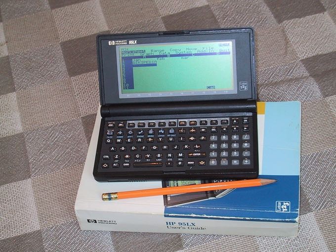 Um modelo 1991 do HP 95LX, junto ao seu manual, que é maior que ele.