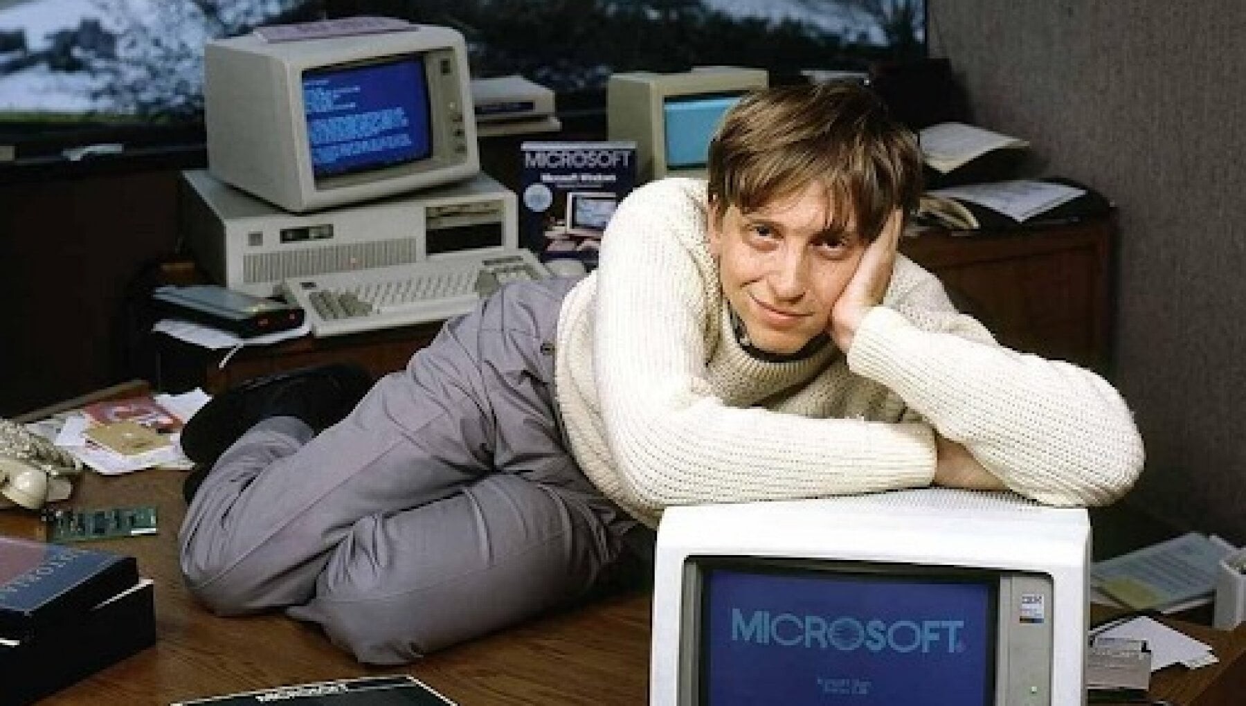 Bill Gates, sem óculos, sobre um IBM PC mostrando o logo da Microsoft