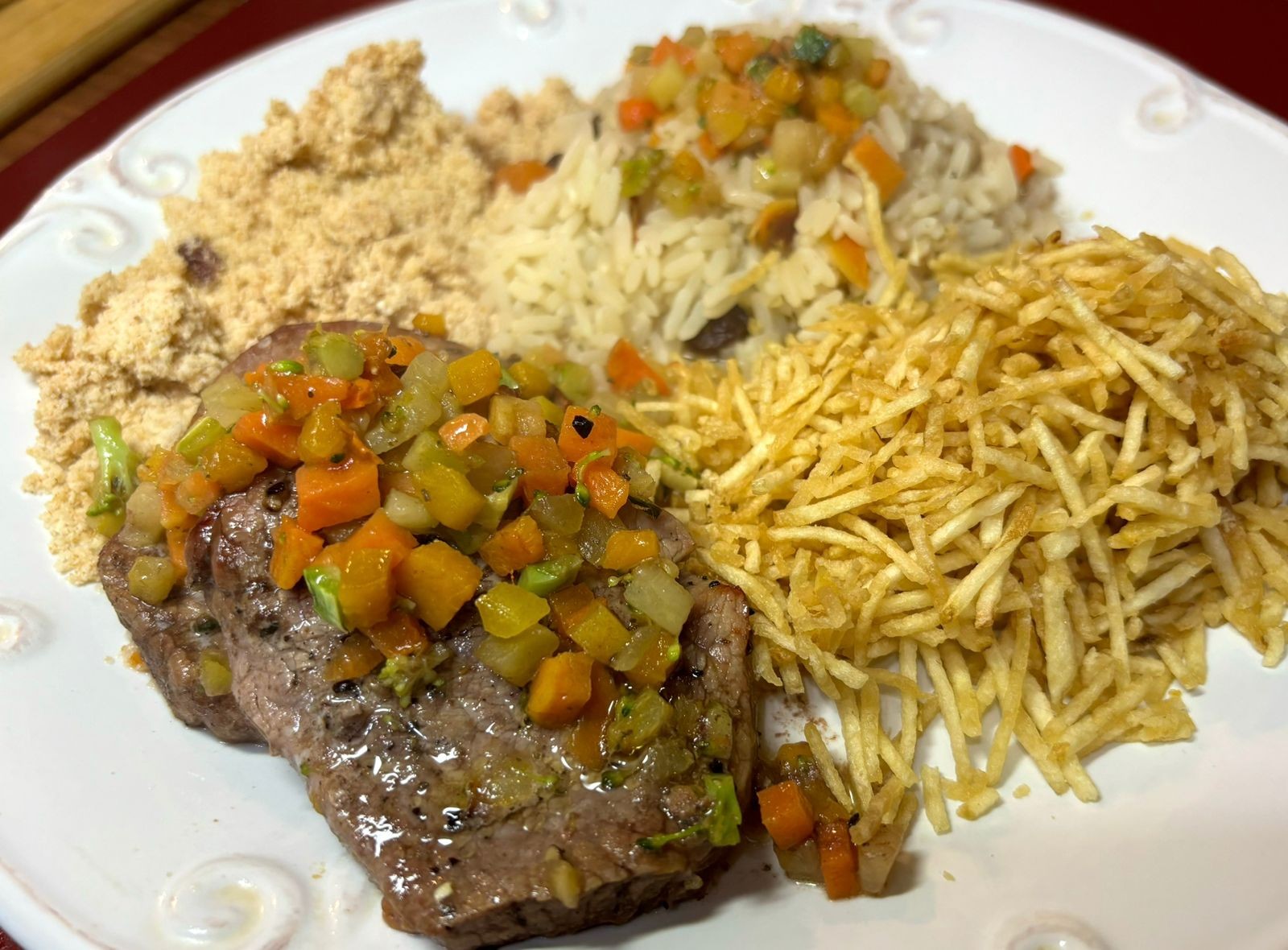 Foto de um prato de refeição, ainda intocado, contendo bife, arroz à grega, farofa e batata palha