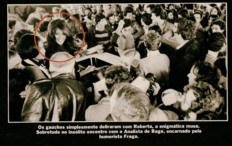 Foto jornalística de Roberta Close cercada da multidão no aeroporto de Porto Alegre, e a legenda: “Os gaúchos simplesmente deliraram com Roberta, a enigmática musa. Sobretudo no insólito encontro com o Analista de Bagé, encarnado pelo humorista Fraga.“