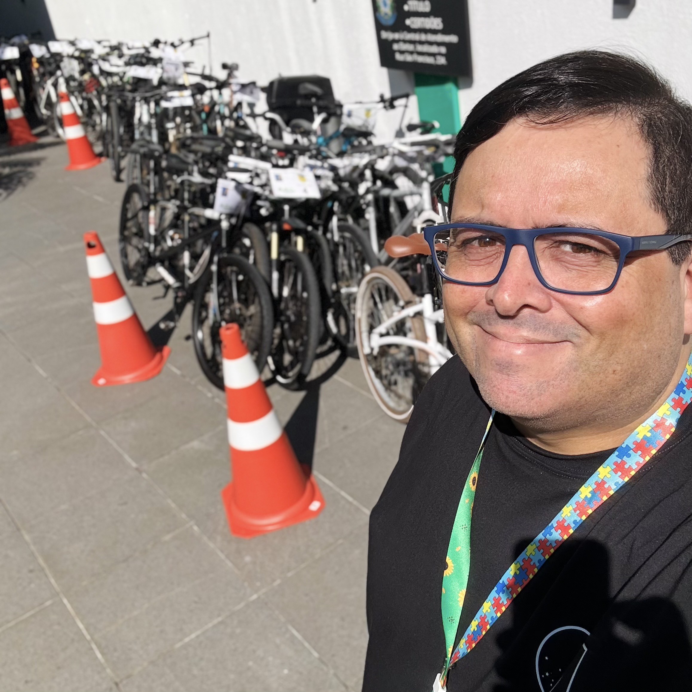 Selfie minha com cordão de identificação de autismo, tendo ao fundo dezenas de bicicletas ao sol