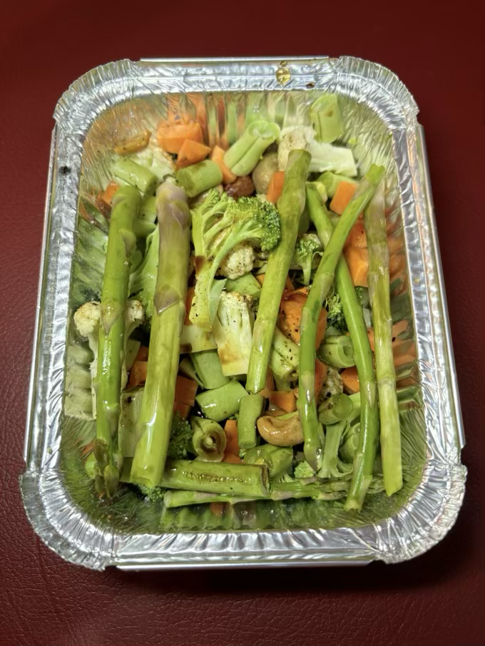 Uma embalagem de alumínio contendo legumes picados em cubinhos e alguns ramos de aspargo, todos ainda crus