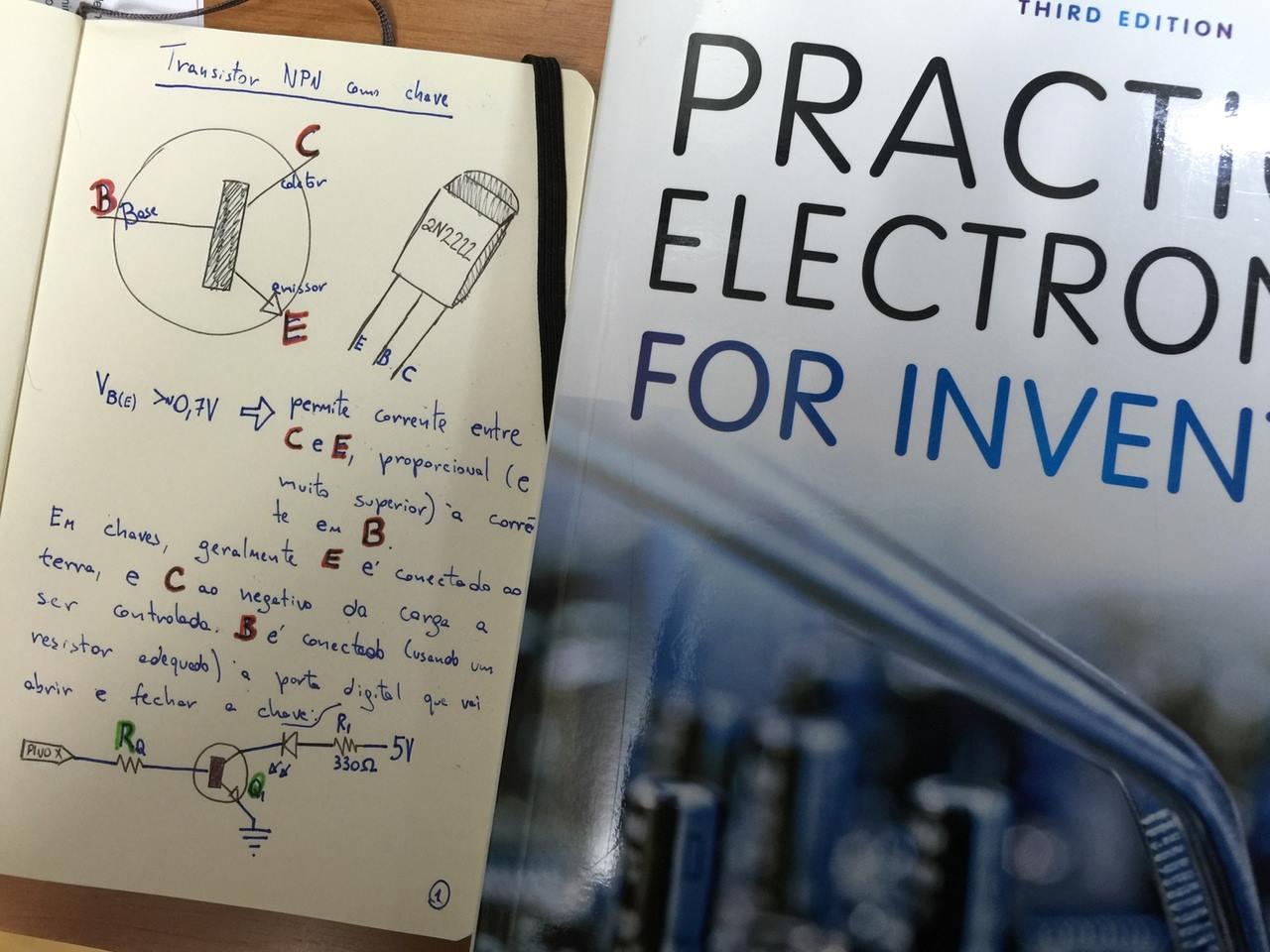 Ao lado da capa do livro Practical Electronics for Inventors, um bloco de anotações aberto em uma página escrita por mim com desenho e diagrama do transistor 2N2222, e apontamentos sobre o seu uso chave.