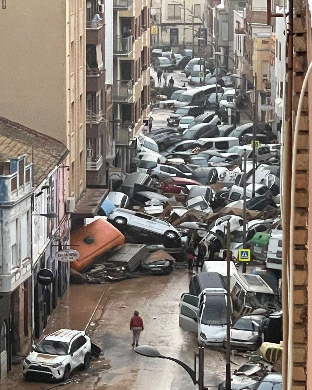 Pedestre observa várias dezenas de carros jogados uns sobre os outros em uma rua de Valencia, na Espanha, para onde foram arrastados após a enxurrada