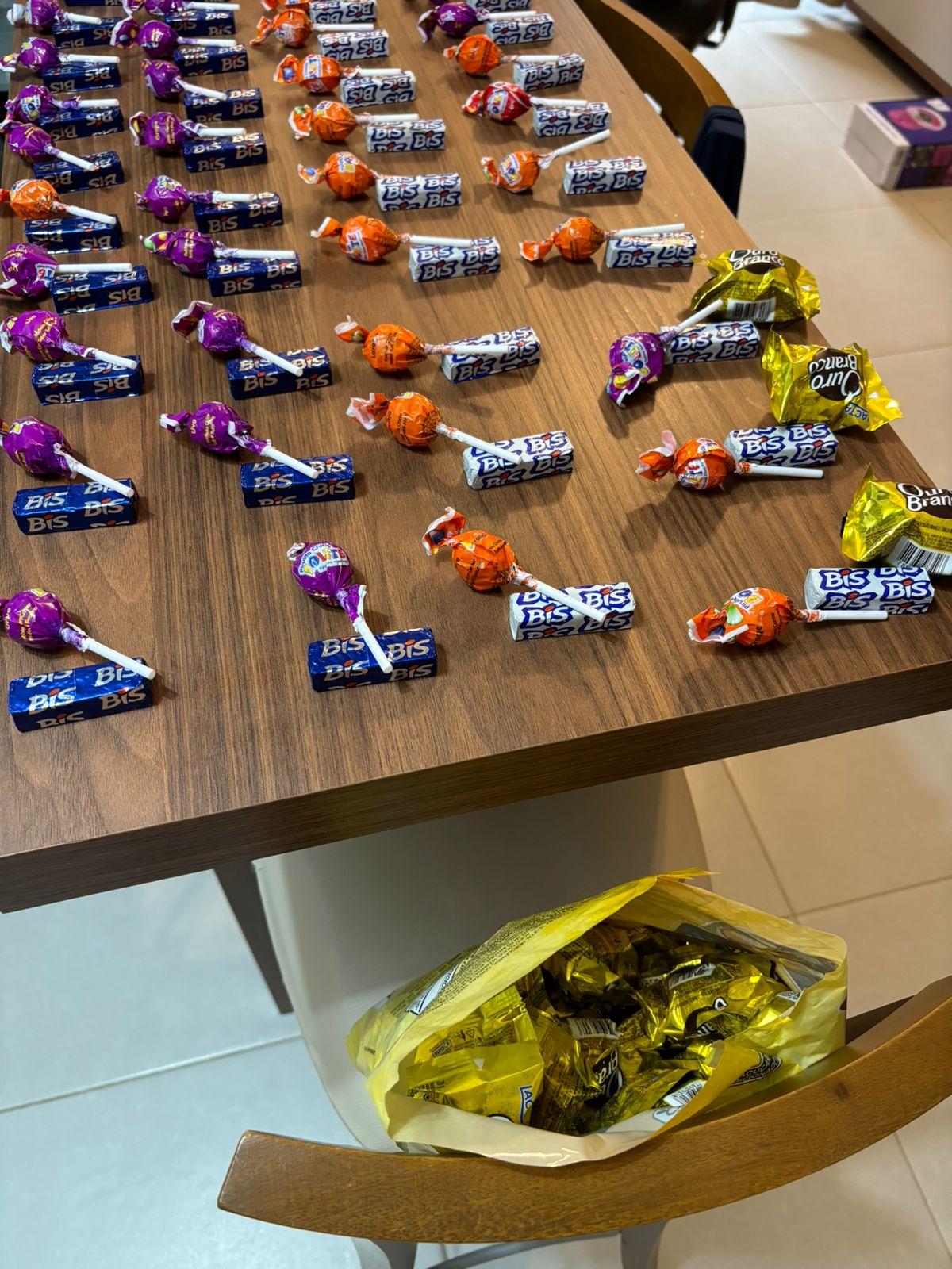 Sobre a mesa estão 40 pequenos grupos de chocolatinhos e pirulitos, aos quais no momento da foto estava sendo adicionado mais um chocolate.