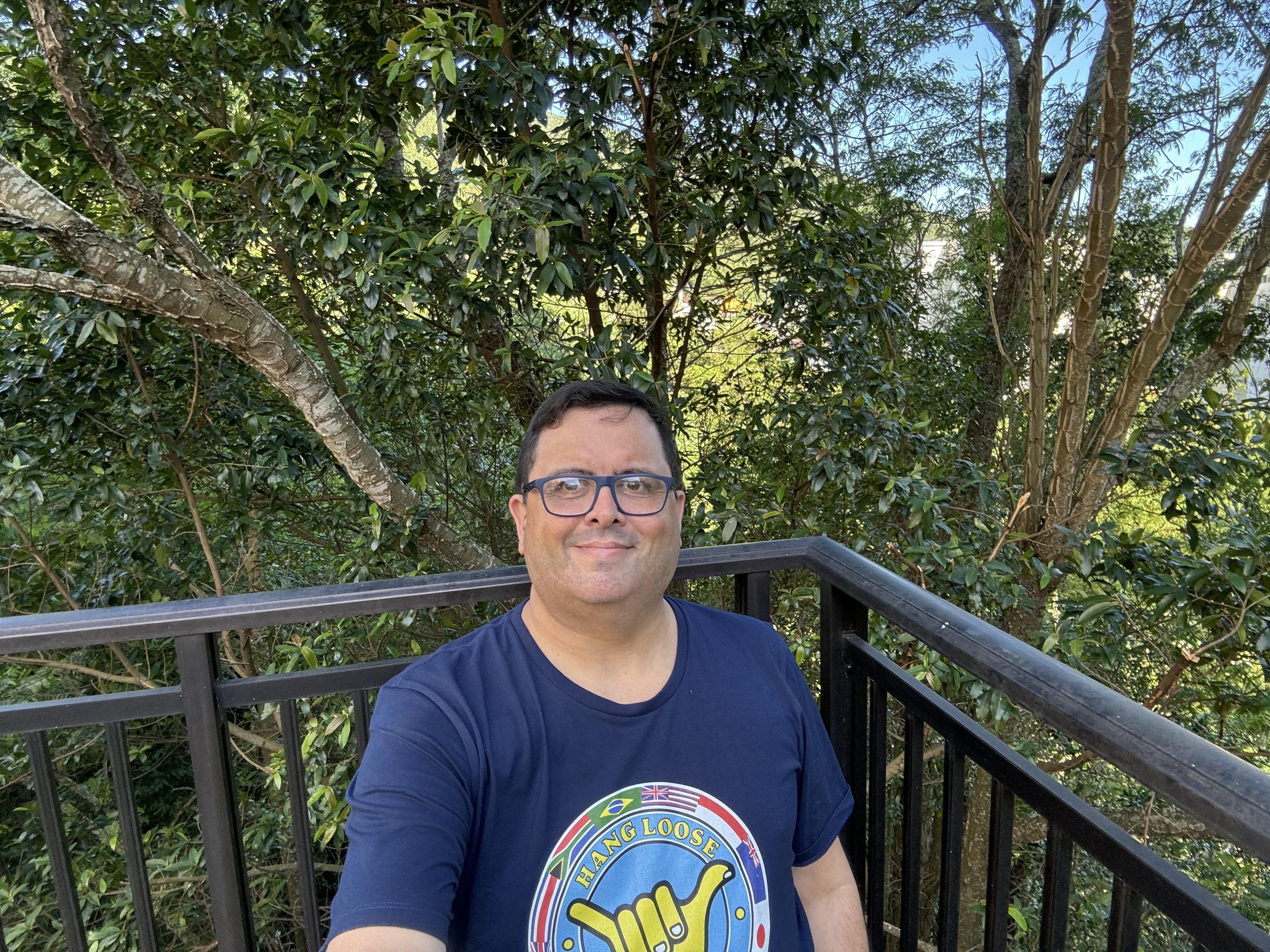 Eu olhando para a câmera e usando uma camiseta com estampa do Hang Loose Pro Contest de 1986, tendo ao fundo a mata