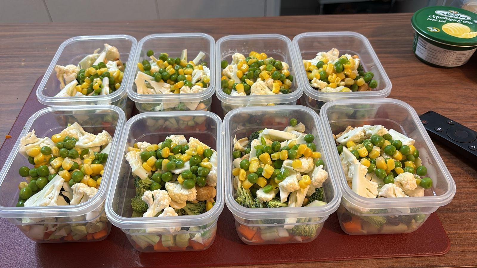 8 potes herméticos abertos, cada um deles contendo cenoura, vagem, brócolis, couve-flor, amendoim, castanha de caju, milho e ervilha
