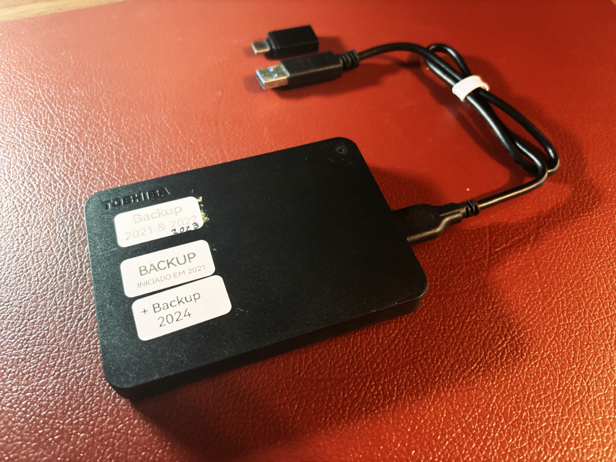 Foto de um HD externo Toshiba com 3 etiquetas indicando que ele armazena backups de 2021, 2022, 2023 e 2024.