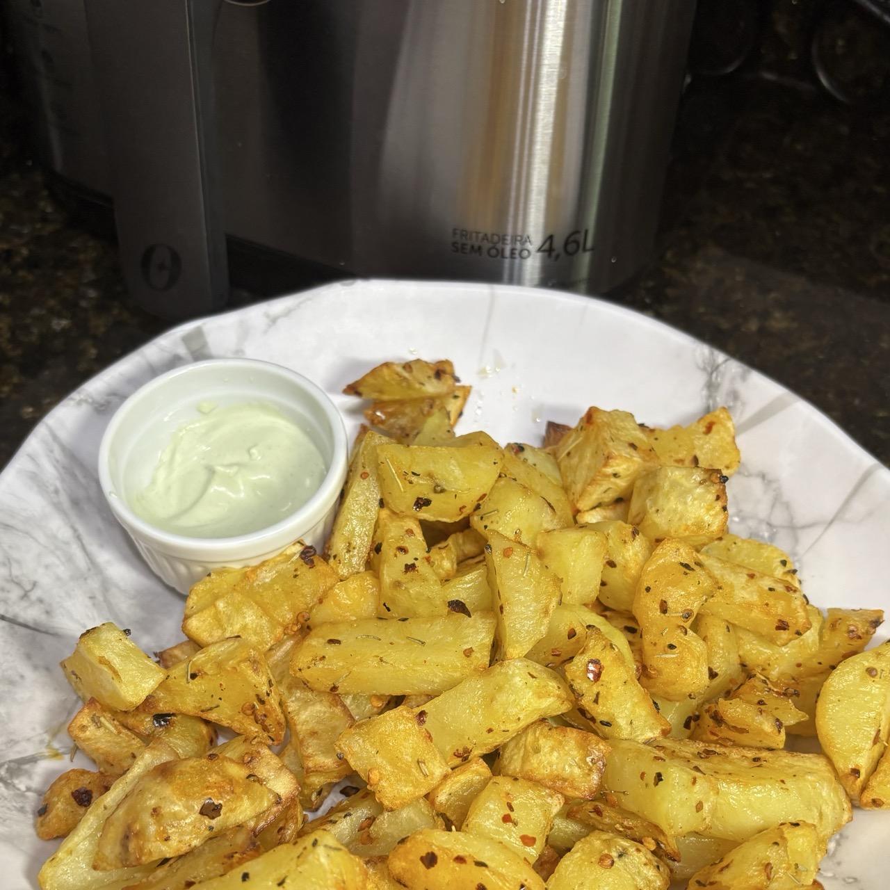 Uma travessa com cerca de 600g de batatas, cortadas, douradas, temperadas e prontas para consumo. Ao fundo é possível ver parte da air fryer.