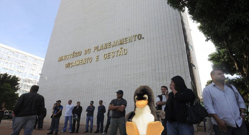O mascote Tux entre um conjunto de pessoas ao lado do prédio do Ministério do Planejamento