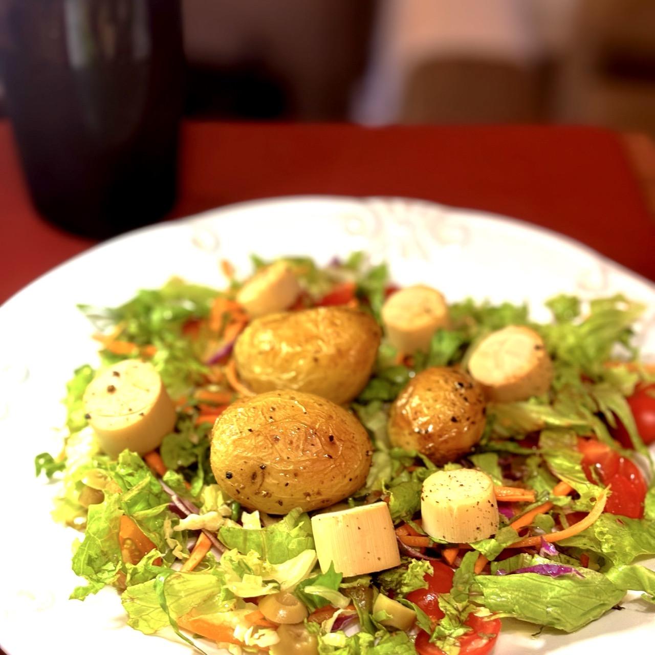 Foto de um prato de salada (descrita no post) sobre a minha mesa, com um copo de líquido ao fundo, desfocado. 