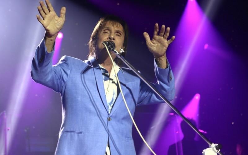 Com braços erguidos e as duas mãos espalmadas, Roberto Carlos gesticula de olhos fechados no palco.