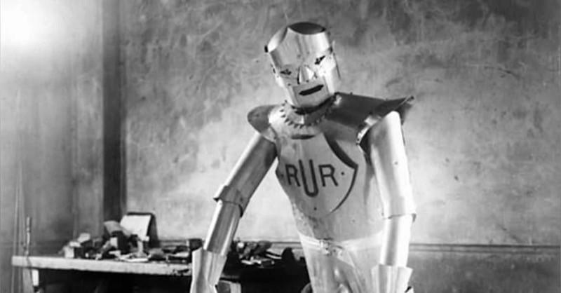 Ator interpreta um robô com o logotipo da empresa RUR, em foto em preto e branco