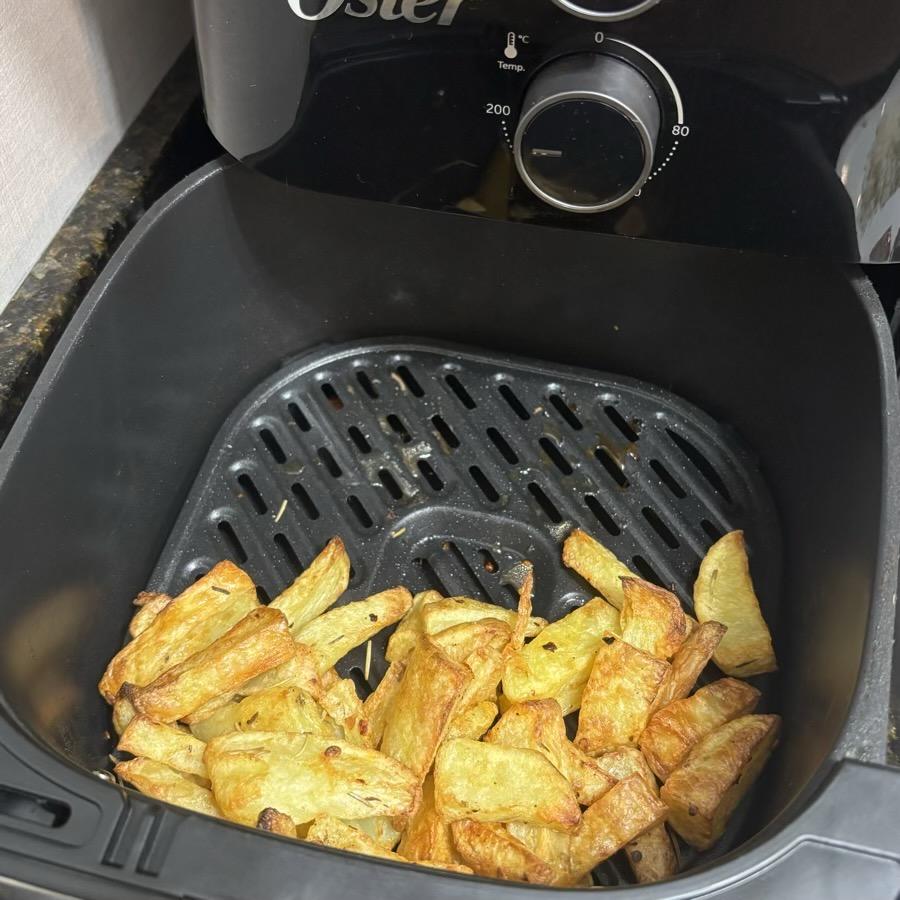 Foto da minha air fryer aberta, parcialmente tomada por batatas fritas já prontas e bem sequinhas e douradas.