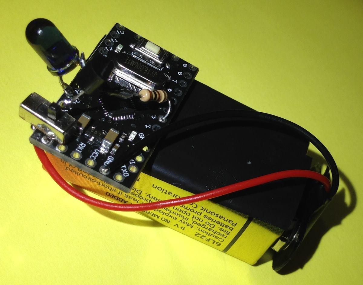 Montagem bem crua de uma chave liga/desliga soldada na conexão entre uma bateria de 9V e um Arduino Pro, ao qual também estão conectados um led infravermelho, um transistor (acho que 2N2222) e um resistor.