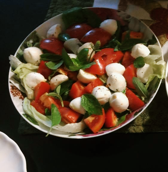 Um prato de salada feita com tomate cortado em pedaços, queijo branco e folhas de manjericão