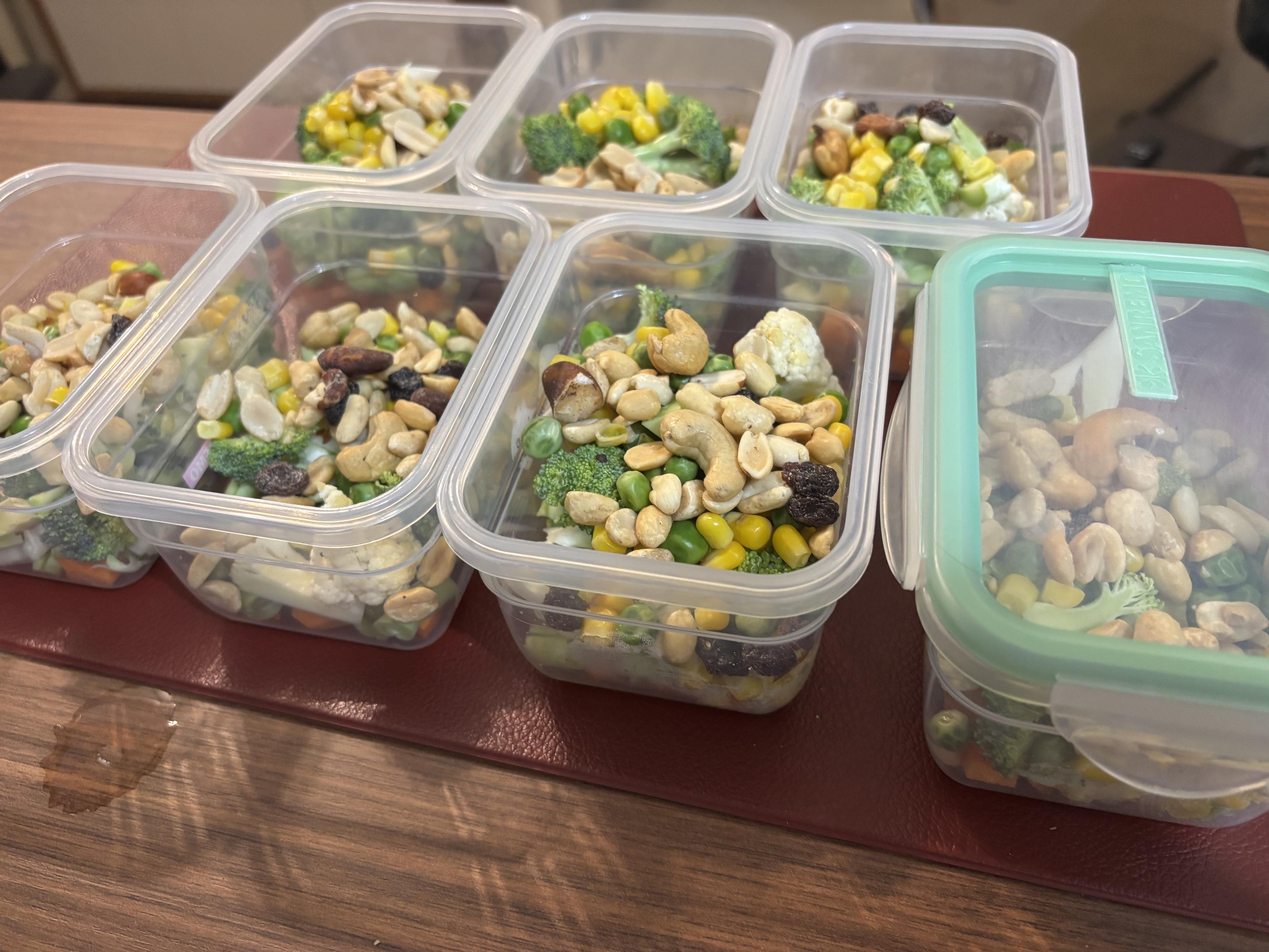 7 pores herméticos idênticos, cada um contendo uma porção de legumes e castanhas. Um deles já está tampado. 