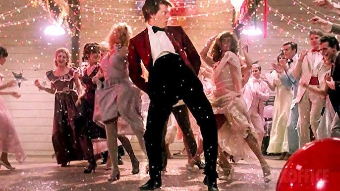 Kevin Bacon, em traje de gala, dança no baile da cena apoteótica do filme Footloose.