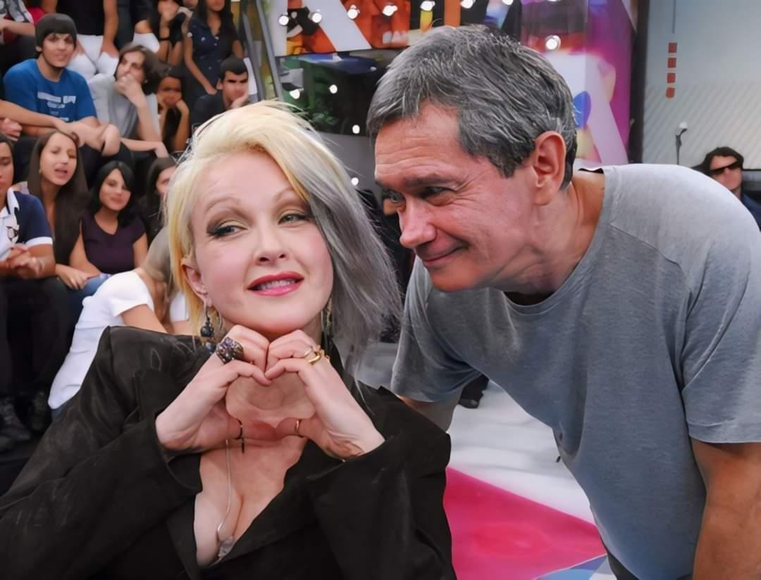 Ao lado de Serginho Groisman, Cyndi Lauper faz um gesto de coração com as mãos no palco do Altas Horas.