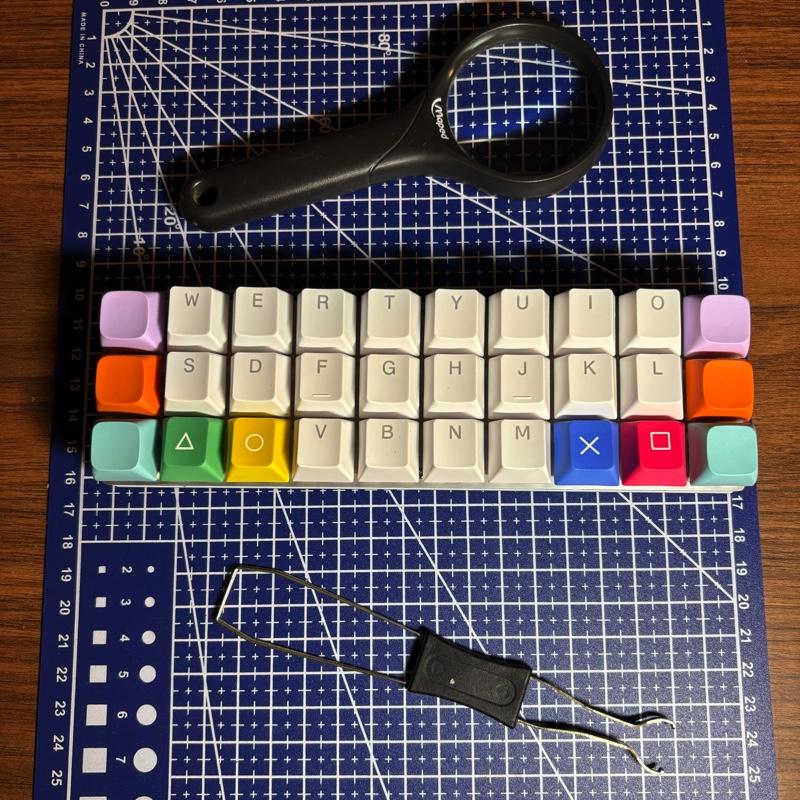 Foto de um teclado originalmente com apenas 30 teclas (só letras e alguns sinais de pontuação, sem números, enter, barra de espaço, shift, etc.), das quais as teclas das extremidades direita e esquerda foram substituídas por teclas coloridas (dois conjuntos de verde, laranja e lilás), e outras quatro teclas foram substituídas por teclas com os símbolos geométricos do controle do playstation: triângulo, círculo, x e quadrado.