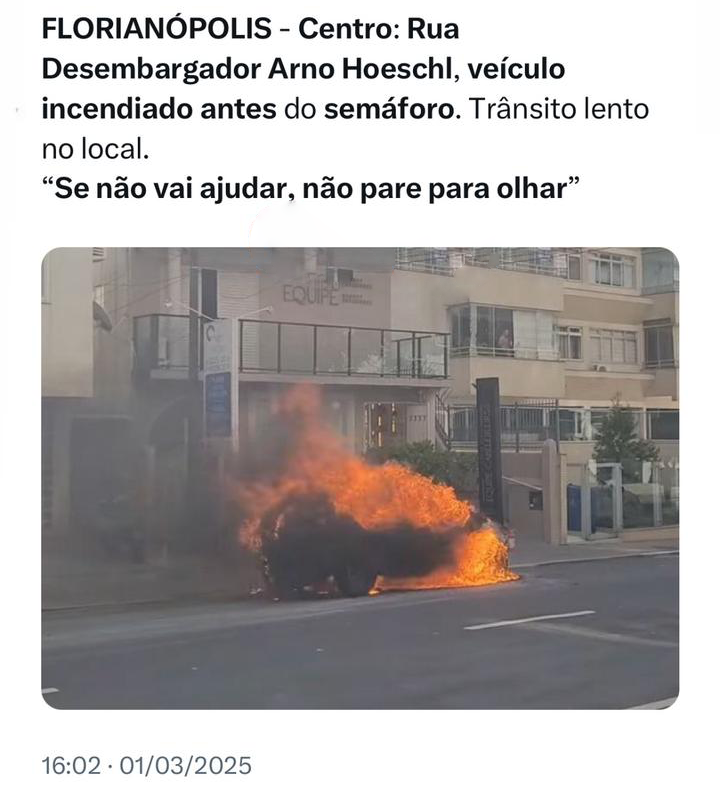 Foto de um carro de pequeno porte, estacionado, tomado pelas chamas. O texto diz: <br><br>FLORIANÓPOLIS - Centro: Rua Desembargador Arno Hoeschl, veículo incendiado antes do semáforo. Trânsito lento no local.<br>“Se não vai ajudar, não pare para olhar“