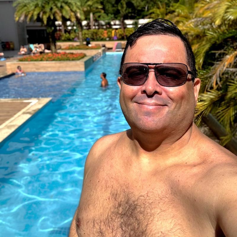 foto minha, sem camisa, cabelo molhado, de óculos escuros, em cena ensolarada, tendo ao fundo a piscina e a vegetação