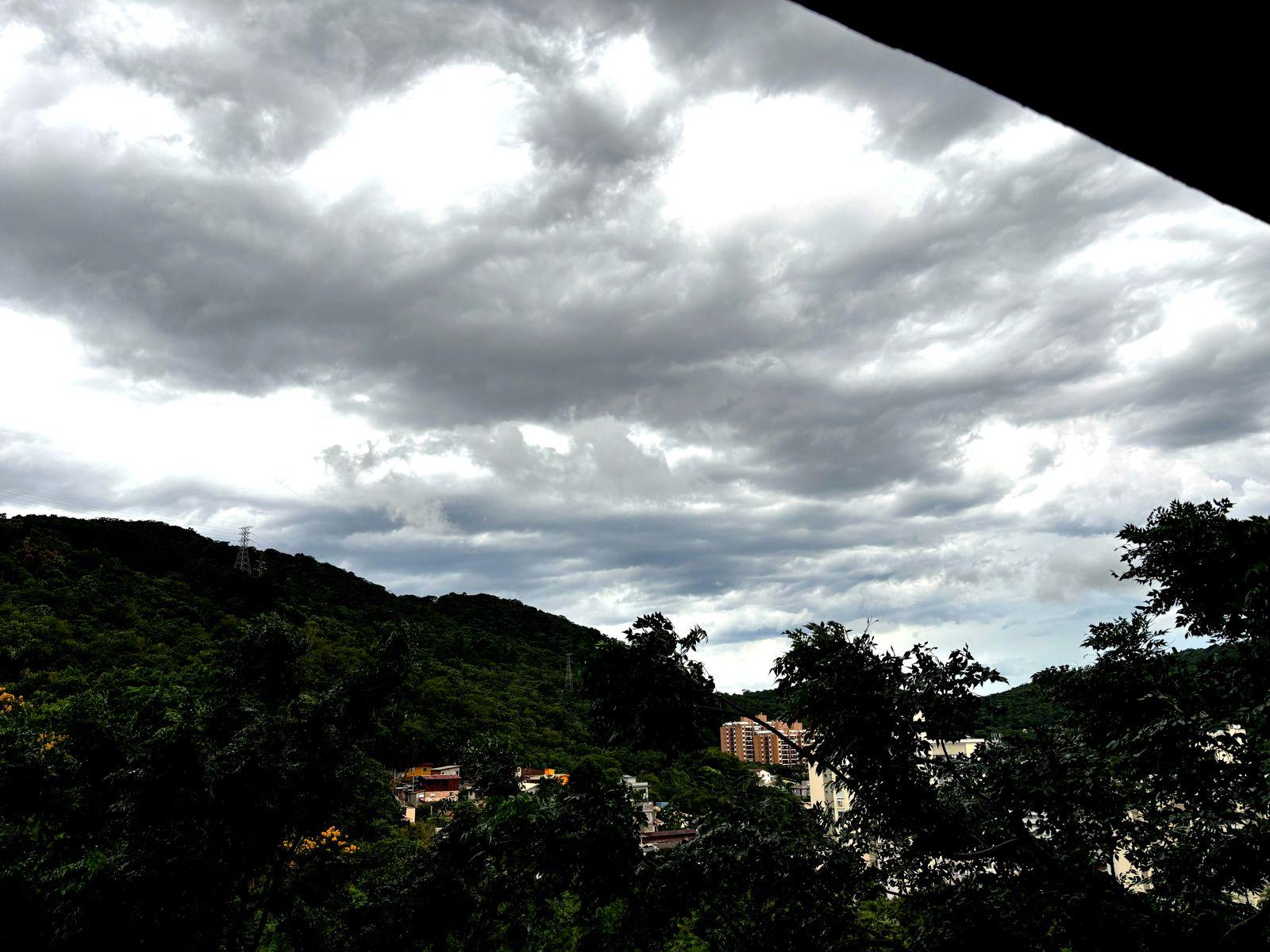 Foto tirada da minha janela, mostrando o céu tomado por nuvens cinzas, emolduradas pela mata do Morro da Lagoa