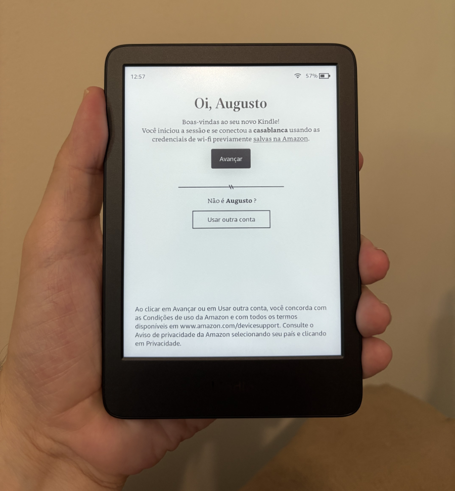 Um Kindle, aproximadamente do tamanho da minha mão que o segura. A tela dele mostra uma mensagem de configuração inicial, com 2 botões que podem ser pressionados diretamente na própria tela.