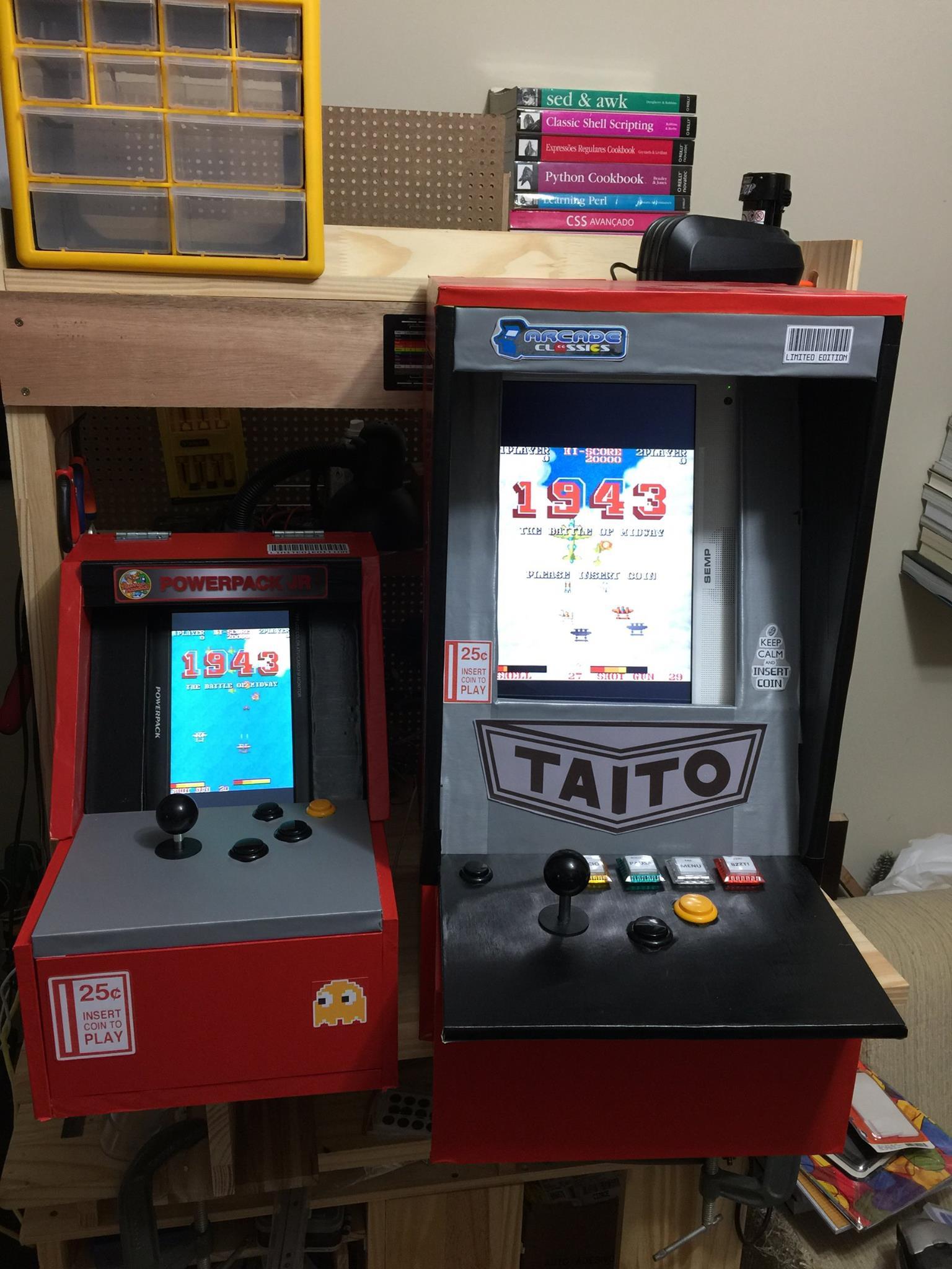 duas máquinas de fliperama, sendo uma com cerca de 60cm de altura, e a outra um pouco maior, feitas com técnicas de marcenaria. Ambas estão na minha bancada de trabalho, cada uma delas tem uma alavanca de comando, 2 botões de jogo e mais alguns botões de controle. As duas exibem telas do jogo 1943, no momento da foto.<br><br>